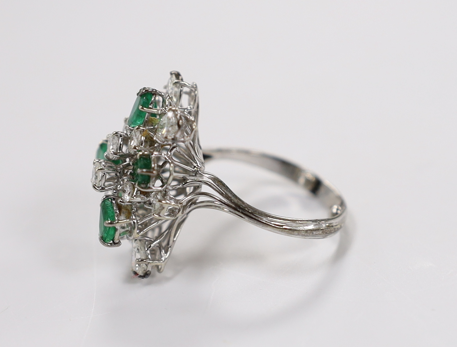 A modern white metal emerald and diamond cluster set dress ring, size R/S, the shank with two sizing spheres, gross weight 8 grams.